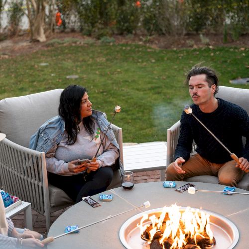 People are sitting around an outdoor fire pit, toasting marshmallows on sticks, enjoying a relaxed gathering.