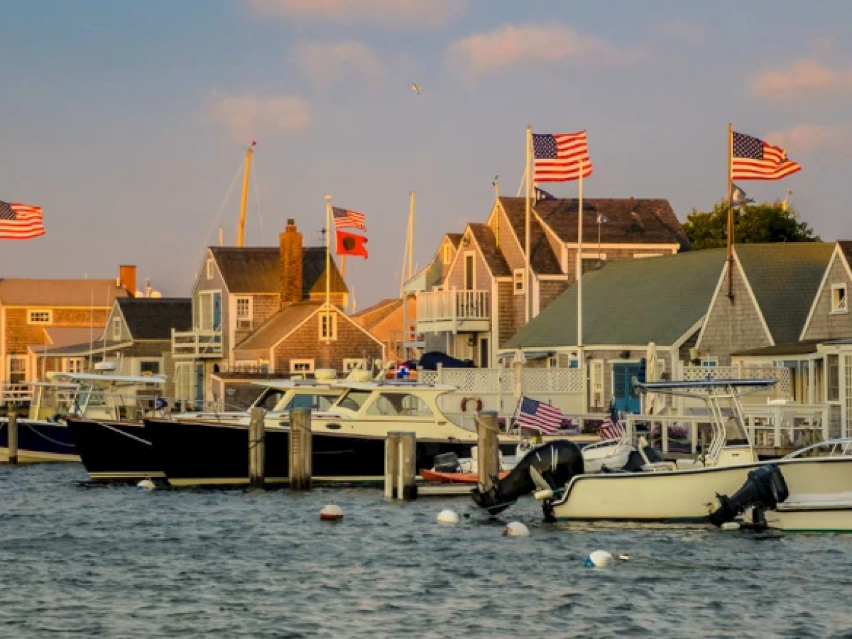 A coastal scene with boats docked at a marina and houses in the background, adorned with American flags.