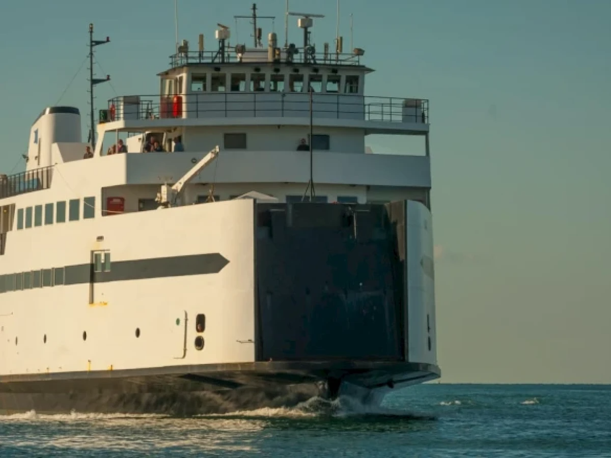 A large ferry is moving through the water, with its bow breaking the waves under a clear sky.