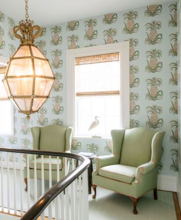 A cozy stair landing with a hanging lantern light, pineapple-pattern wallpaper, and two green chairs near the windows.