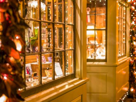 Warmly lit storefront window with fairy lights, ornaments, and greeting cards in a cozy holiday scene.