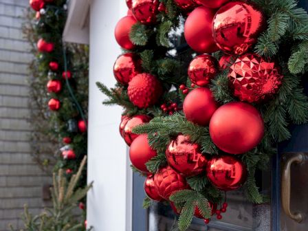 A festive holiday wreath packed with shiny red and metallic ornaments and evergreen branches on a building doorway, ready for Christmas celebrations.