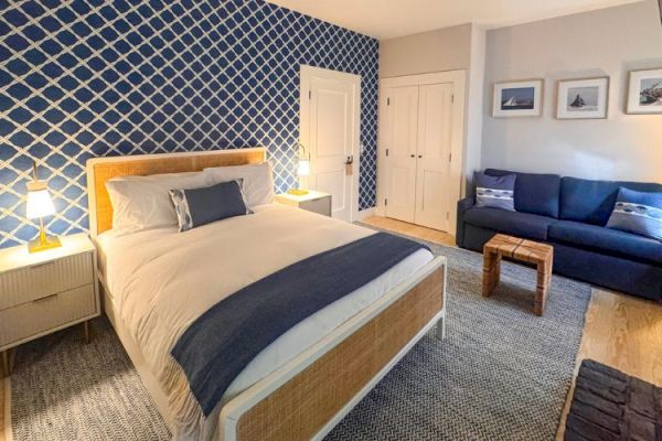 A cozy bedroom with a bed, blue-patterned accent wall, sofa, nightstands, and framed artwork. Warm lighting enhances the serene ambiance.