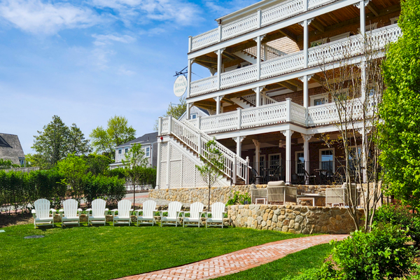 Large building with multiple wooden balconies, green lawn, white chairs, and a stone pathway under a blue sky.
