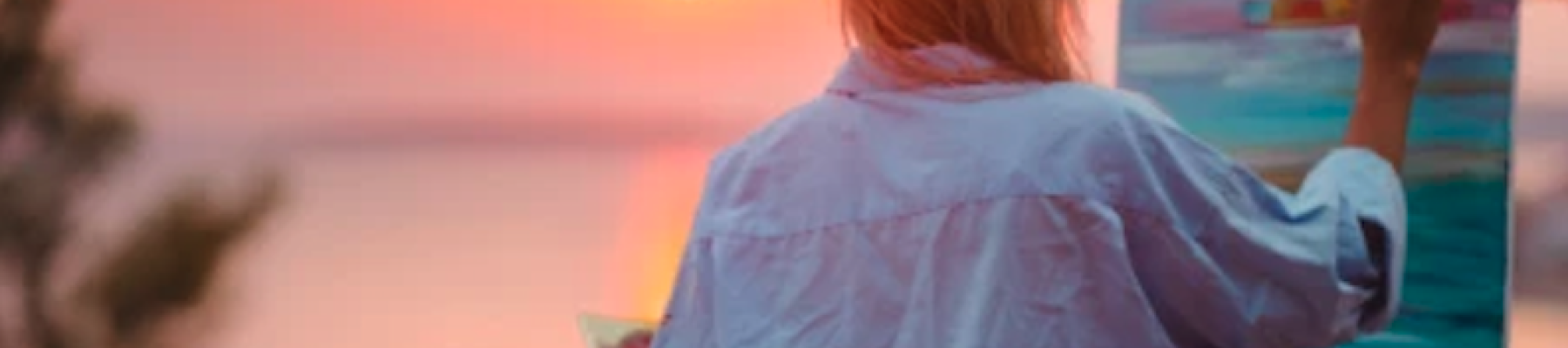 A person is painting on a canvas during a sunset, with a vibrant sky and blurred natural landscape in the background.