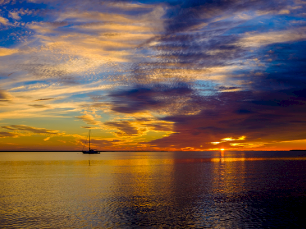A sailboat on calm water during a vibrant sunset with colorful clouds in the sky.
