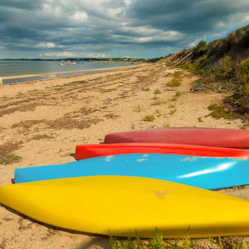 The image shows kayaks on a sandy beach with a cloudy sky and distant shoreline.