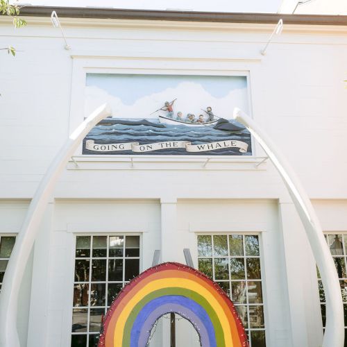 A mural shows people rowing a whale with a banner reading &ldquo;GOING ON THE WHALE,&rdquo; inside a white building entrance.