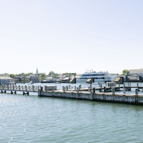 A Seastreak ferry sits at a harbor dock beside piers, mooring posts, and waterfront buildings under a cloudy sky.
