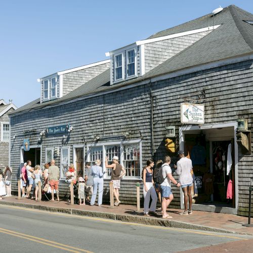 People line up at a seaside building with signs for &ldquo;The Sunken Ship&rdquo; and &ldquo;The Juice Bar&rdquo; on a sunny day.