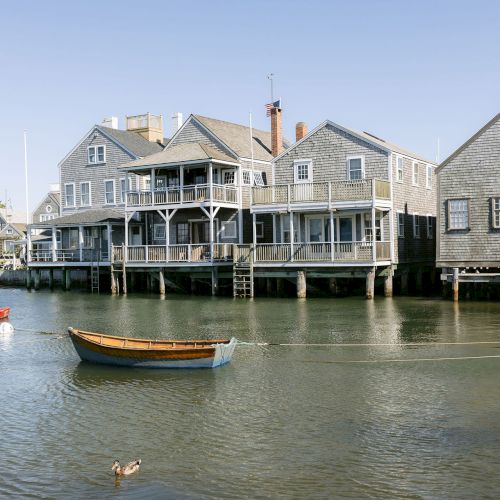 Waterfront homes on wooden docks with boats on calm water, and a small U.S. flag flying above the roof.