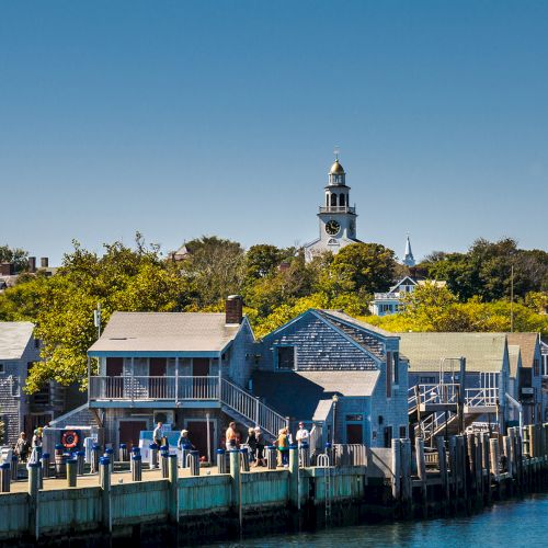 A picturesque coastal town with charming buildings, a dock, and a prominent tower under a clear blue sky.