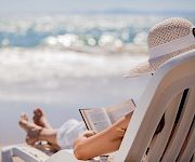 A person lounging on a beach chair by the ocean, reading a book, wearing a sunhat, with waves and sunlight in the background. End.