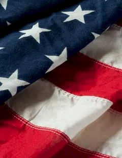 A close-up of an American flag fabric, showing blue with white stars and red-and-white stripes in soft folds.