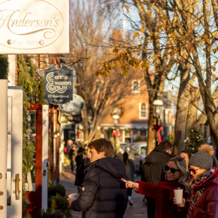 A busy small-town street with shops and holiday signs, people in winter coats walking under bare trees.